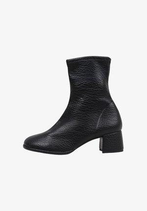 Bota de cuero negro hasta el tobillo con un acabado texturizado, puntera cuadrada y un bajo tacón en bloque. Los detalles de costura añaden estructura al diseño.