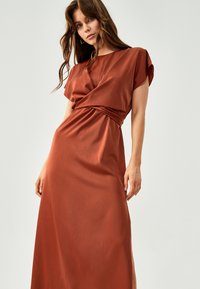 Cimetno obarvana maxi obleka z zavitim dizajnom, kratkimi rokavi in gladko satensko teksturo, ki ima detajl z zgrnjenim pasom.