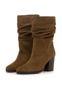 Botas de tobillo de ante marrón con un diseño holgado, punta cónica y tacón de madera apilada. Textura suave con una estética minimalista.