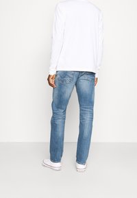 Blue denim jeans with a straight fit, featuring a faded wash and two back pockets. Paired with a white long-sleeve shirt and white sneakers.