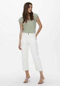 Top corto de color verde claro con mangas cortas, combinado con jeans blancos de pierna recta de tiro alto. Sandalias de tacón transparente completan el atuendo.