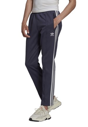 Navy athletic trousers made of woven fabric, featuring white side stripes and an elastic waistband, with side pockets for storage.