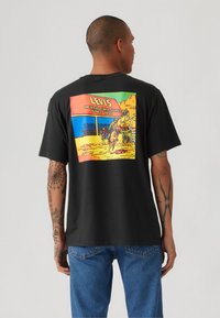 Svart bomulls t-skjorte med et fargerikt grafisk motiv på baksiden som skildrer en vestlig scene, med "LEVI'S" og tekst i fete bokstaver.