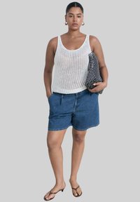 Débardeur tricoté blanc, short en jean, sac noir à motifs et sandales. La tenue présente un style décontracté et confortable avec des textures variées.