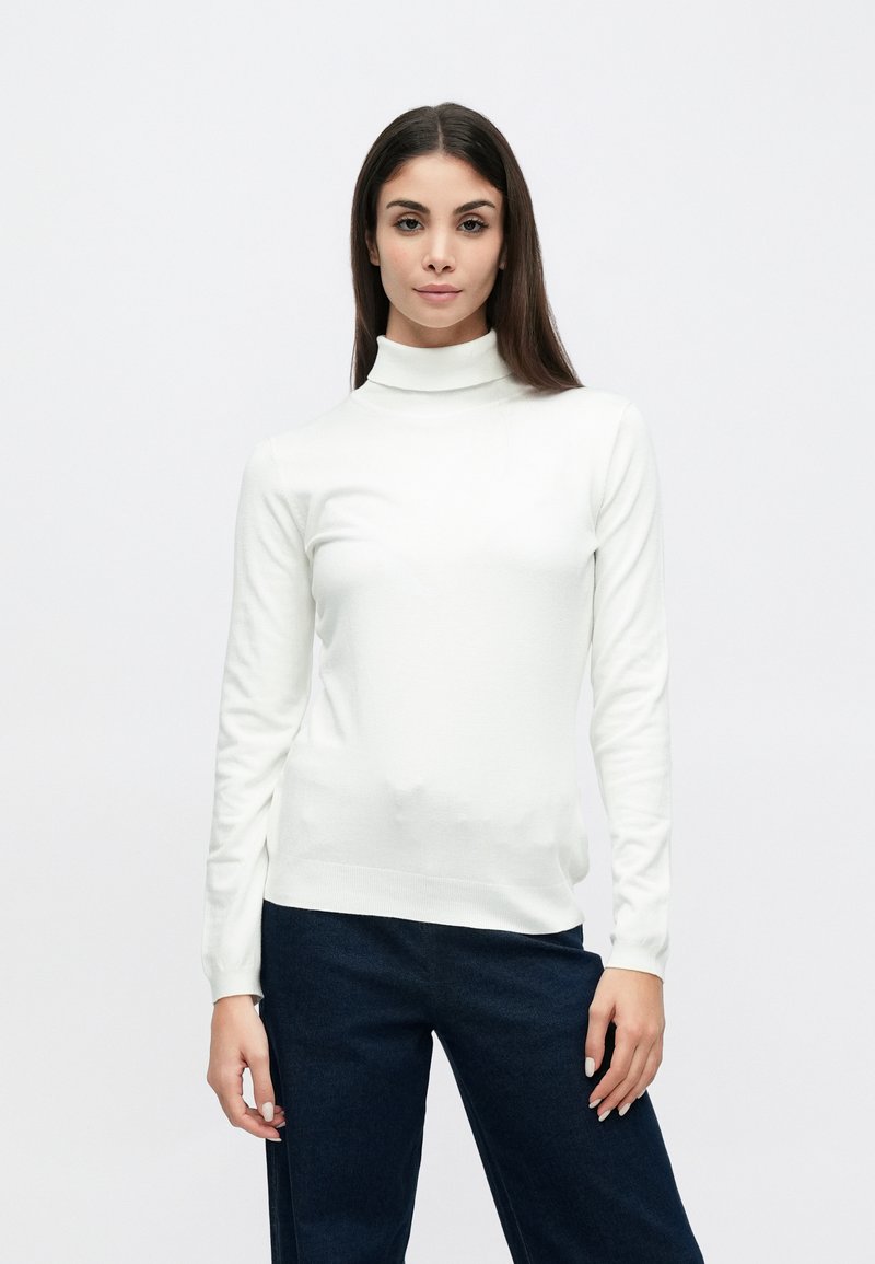 Λευκό πουλόβερ με ζιβάγκο από ελαφρύ ύφασμα, με μακριά μανίκια και εφαρμοστή γραμμή, συνδυασμένο με σκούρο μπλε τζιν παντελόνι.