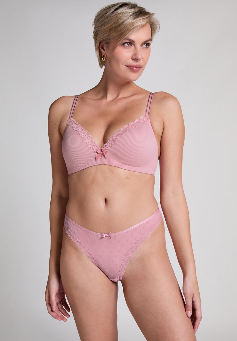 Roze lingerie set met een geribbelde bralette met kantafwerking en een klein strikje, gecombineerd met bijpassende sheer slipjes met hartjespatronen.