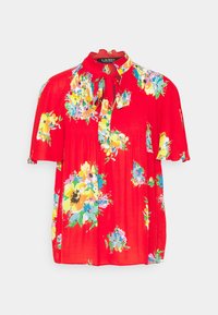 Röd blus med korta ärmar, blommönster i gult, blått och grönt, plisserad textur och en knytning vid halsen.