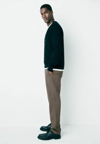 Cardigan negru cu nasturi, cămașă albă cu gât rotund dedesubt, pantaloni bej și pantofi negri. Profil lateral pe un fundal simplu.