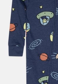 Navy fabric jumpsuit featuring space-themed print with planets, stars, and UFOs. Designed with a zipper and ribbed cuffs. Soft texture.
