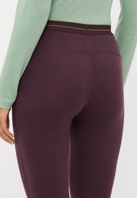 Høyt livde lilla leggings laget av et fleksibelt materiale, med en glatt tekstur og kontrasterende mørk livlinje med en subtil sømdetalj.