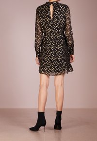 Robe noire avec un motif floral doré, manches longues transparentes, taille cintrée et un détail en forme de trou de serrure au dos. Associée à des bottines noires.