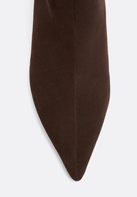 Ruskean mokkanahkainen solmio, jossa on terävä kärki, sileä pinta ja hienovarainen kiilto. Ei näkyviä kuvioita tai metalliosia. Yksinkertainen ja tyylikäs muotoilu.