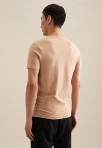 T-shirt en coton beige clair à manches courtes avec col rond, présentant une silhouette ajustée et une texture douce. Coutures minimales visibles à l'arrière.