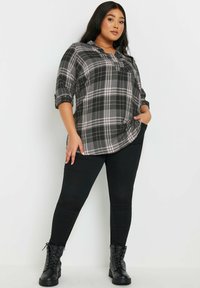 Camicia a quadri grigia e nera con maniche arrotolate, abbinata a jeans skinny neri e stivaletti in pizzo neri. Tessuto liscio, design informale.