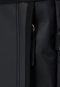 Poche en tissu noir avec un stylo noir fin partiellement inséré verticalement à l'intérieur de la poche.