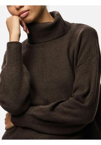 Maglione a collo alto marrone realizzato in morbido tessuto texturizzato, con polsini e colletto a coste, caratterizzato da una vestibilità rilassata e da dettagli di cucitura sottili.