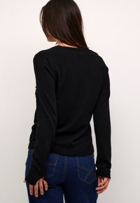 Suéter negro de punto con mangas largas, diseño ajustado y puños acanalados, combinado con jeans de mezclilla que cuentan con bolsillos traseros y costuras azules.