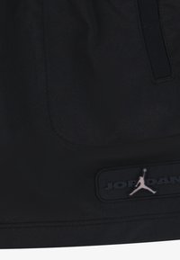 Černé sportovní šortky s hladkým povrchem, obsahující viditelnou kapsu a texturovanou nášivku loga JORDAN. Jednoduchý design, bez vzorů.