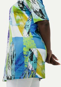 Túnica colorida con patrones abstractos en azul, verde, amarillo y negro. Las mangas cortas y las aberturas laterales mejoran la circulación de aire y la comodidad.