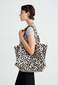 Leopard print tote bag made of soft fabric, featuring a wide open top and sturdy handles. Colors include cream and black.