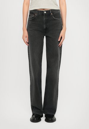 Mujer vistiendo jeans rectos negros de talle alto con bolsillos frontales, combinados con zapatos negros y un top corto a rayas.