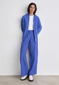 Blue striped button-up shirt paired with matching wide-leg pants, both made of a lightweight fabric. White T-shirt underneath, black platform shoes.