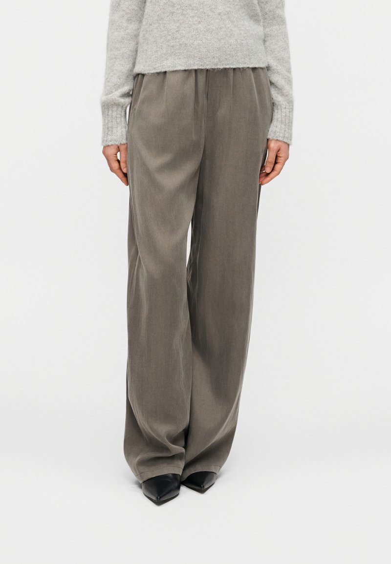 Grey wide-leg trousers with a soft texture, featuring pleats at the front, paired with pointed black shoes and a light grey sweater.