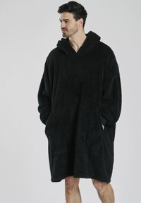 Coperta con cappuccio oversize nera, con una superficie testurizzata e soffice, dotata di tasche frontali e una vestibilità rilassata. Adatta per il relax o per tenerti caldo.