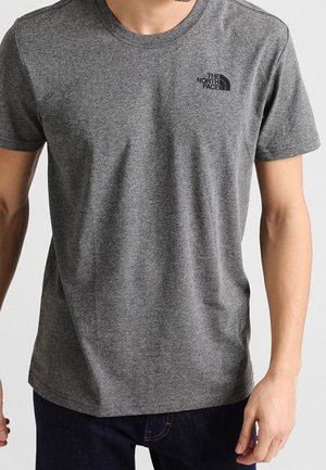Homme portant un t-shirt gris uni à manches courtes avec le logo The North Face sur la poitrine gauche et un jean bleu foncé.