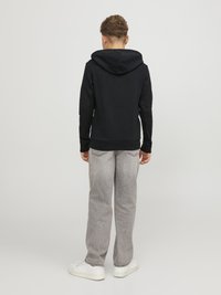 Črna kapuca s sweatshirtom z gladko teksturo, nosi se z svetlo sivo jeans hlačami, ki imajo izblajen videz, ter belimi supergami.