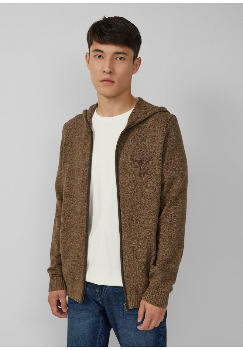 Brauner, strukturierten Reißverschluss-Hoodie mit Kängurutasche und besticktem Design, kombiniert mit einem schlichten weißen T-Shirt und blauen Jeans.