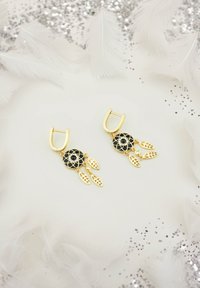 Guldörhängen med svarta cirkulära charm med intrikata spetsmönster, dekorerade med bladdetaljer och små klara stenar.