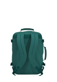 Zaino turchese con spallacci imbottiti, una maniglia superiore e clip laterali. Forma rettangolare e tessuto testurizzato offrono durabilità.