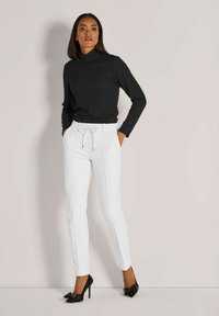 Zwarte textuur turtleneck, witte op maat gemaakte broek met koord, slim fit, en zwarte hoge hakken met strikdetail.