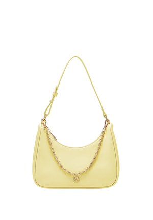 Kleine, blassgelbe Handtasche mit verstellbarem Schulterriemen, goldener Kettendetail und rundem goldfarbenem Anhänger, der von der Kette hängt.