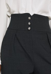 Höga svarta rutiga byxor med en strukturerad passform, som har tre dekorativa knappar framtill och subtila veck.