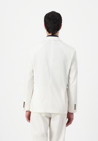 Witte blazer met een getailleerde pasvorm, voorzien van een enkele vent en vier knopen op de mouw, getoond vanaf de achterkant. Glad stoffen textuur.