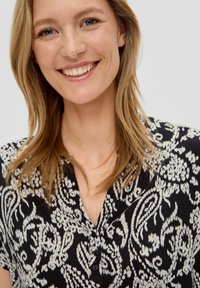 Zwart-witte gebloemde blouse met een kraag, een knoopsluiting aan de voorkant en korte mouwen met een flowy pasvorm.