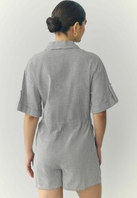 Gestreepte playsuit in zwart en wit met korte mouwen, knoopsluiting bij de kraag, elastische taille en zijzakken. Lichte stof met een gladde textuur.