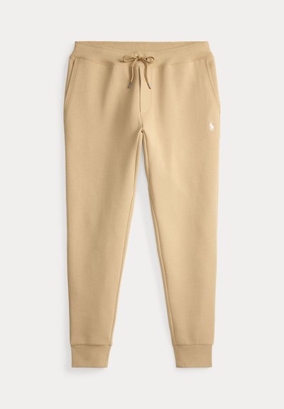 Pantalon de survêtement beige slim-fit avec taille à cordon, poches latérales, poignets côtelés et petit logo blanc brodé sur la cuisse gauche.