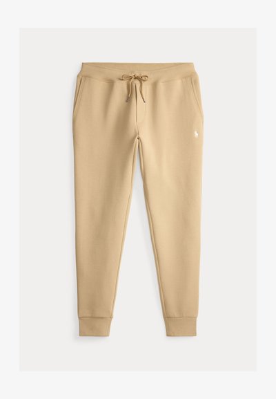 Pantalon de survêtement beige slim-fit avec taille à cordon, poches latérales, poignets côtelés et petit logo blanc brodé sur la cuisse gauche.