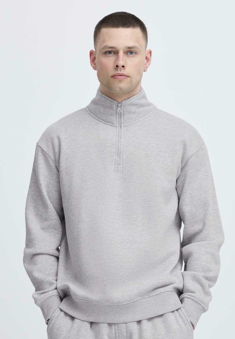 Lys grå, zip-up hettegenser med høy krage og avslappet passform. Myk tekstur, ribbestrikkede mansjetter og et enkelt design uten logoer.
