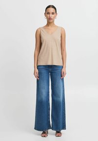 Beige bezrukávový top s výstřihem do V, doplněný o modré džíny s širokými nohavicemi. Džíny mají klasický odstín a volný střih.