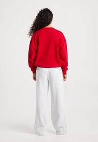 Rode sweatshirt met een ontspannen pasvorm, ronde halslijn en verlaagde schoudernaden, gecombineerd met lichtgrijze sweatpants met een losse snit.