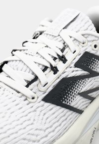 White and gray athletic shoe featuring a textured knit upper, black accents, flat laces, and a structured sole with branding detail.