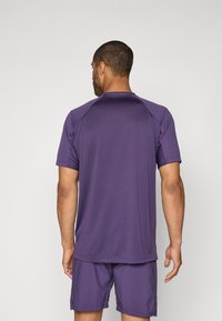 Purple athletic shirt with short sleeves and a round neckline, made of textured material, displayed from the back with matching shorts.