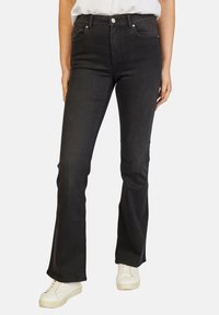 Zwarte flared jeans van denim, met een hoge taille, vijf zakken en subtiele stikdetails, gecombineerd met witte sneakers.