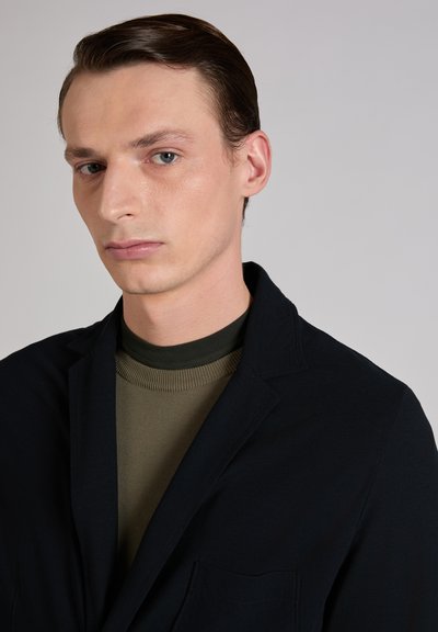 Navy blazer with notched lapels and a single chest pocket, over an olive green ribbed turtleneck. Smooth fabric with tailored fit.