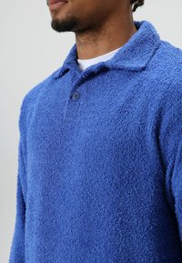 Blauwe fleece trui met een gestructureerd oppervlak, voorzien van een knoopsluiting en een klassieke kraag. Het ontwerp heeft lange mouwen en een losse pasvorm.