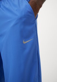 Blue athletic shorts made of smooth fabric. Features include side pockets and a small, gray Nike logo on the lower left side.